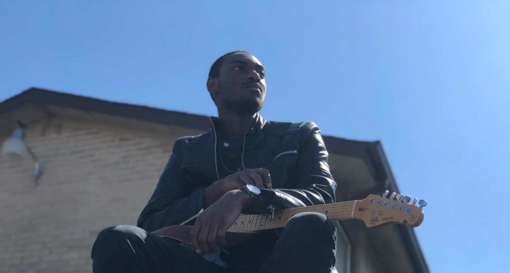 Mathias Lattin poses with guitar and a blue sky background