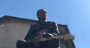 Mathias Lattin poses with guitar and a blue sky background