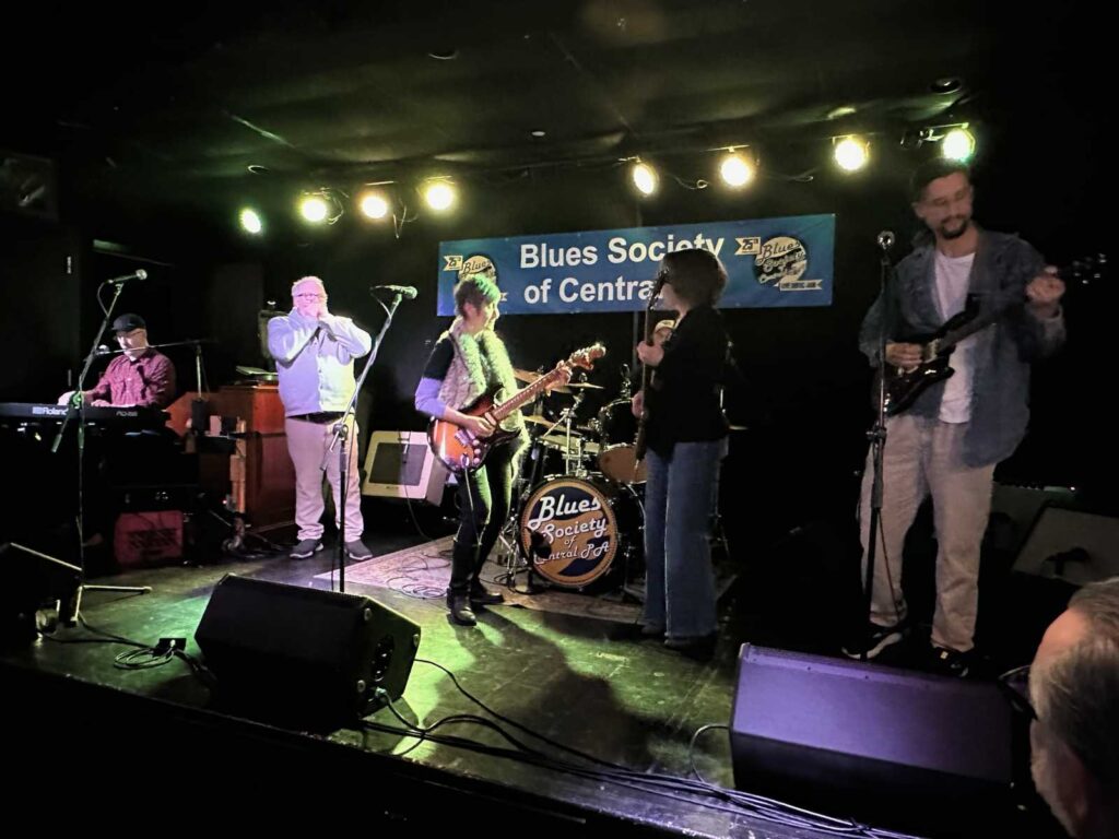 L to R: Tom on keys, Michael Easton on harp, Elise DV on guitar, Jim on drums, Mariana Schaffer on bass, Talll Dave on guitar